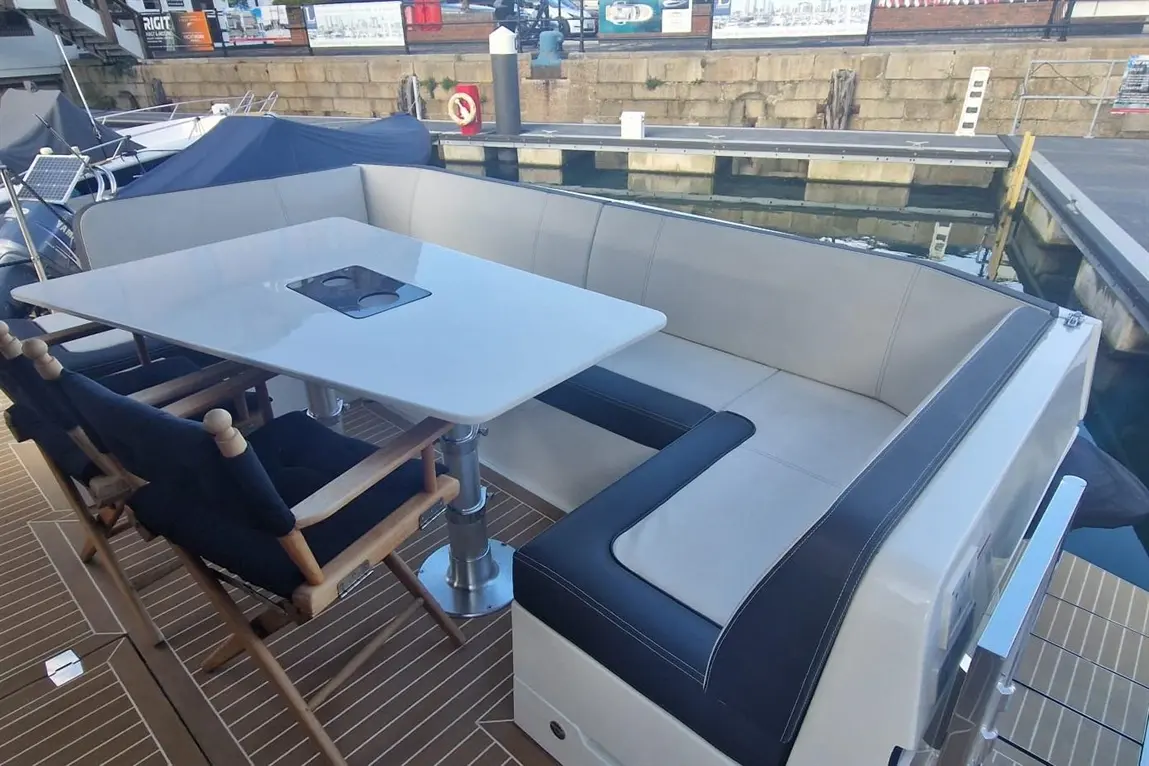 Stylish boat seating area featuring a white table with cup holders and cushioned, navy and cream seats by the marina.